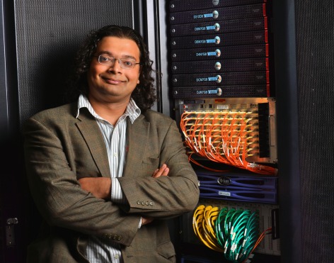 A professor stands beside a supercomputer and its wire components
