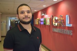 A man in a black polo shirt stands in front of a mechanical engineering sign.