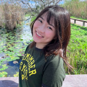A woman in green shirt smiles for photo in front of pond with lillipads.