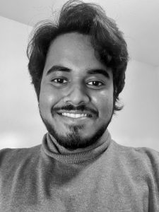 Black and white selfie photo of Suriya N Dhakshinamoorthy smiling at camera