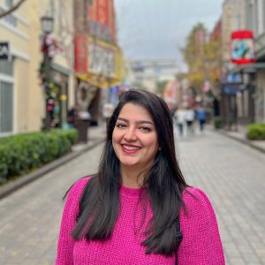 Mozhgan Hadadi smiles for photo in pink sweater standing outdoors on city street.