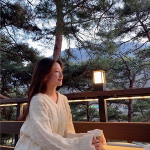 Daeun (Sarah) Kim sits peacefully looking out with a coffee in her hands. Behind her are aspen trees and a mountain range in the far distance.