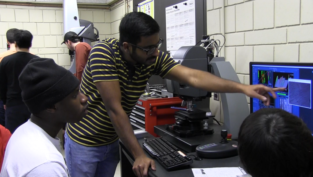 A teaching asssistant works with undergraduate students in the metrology laboratory.