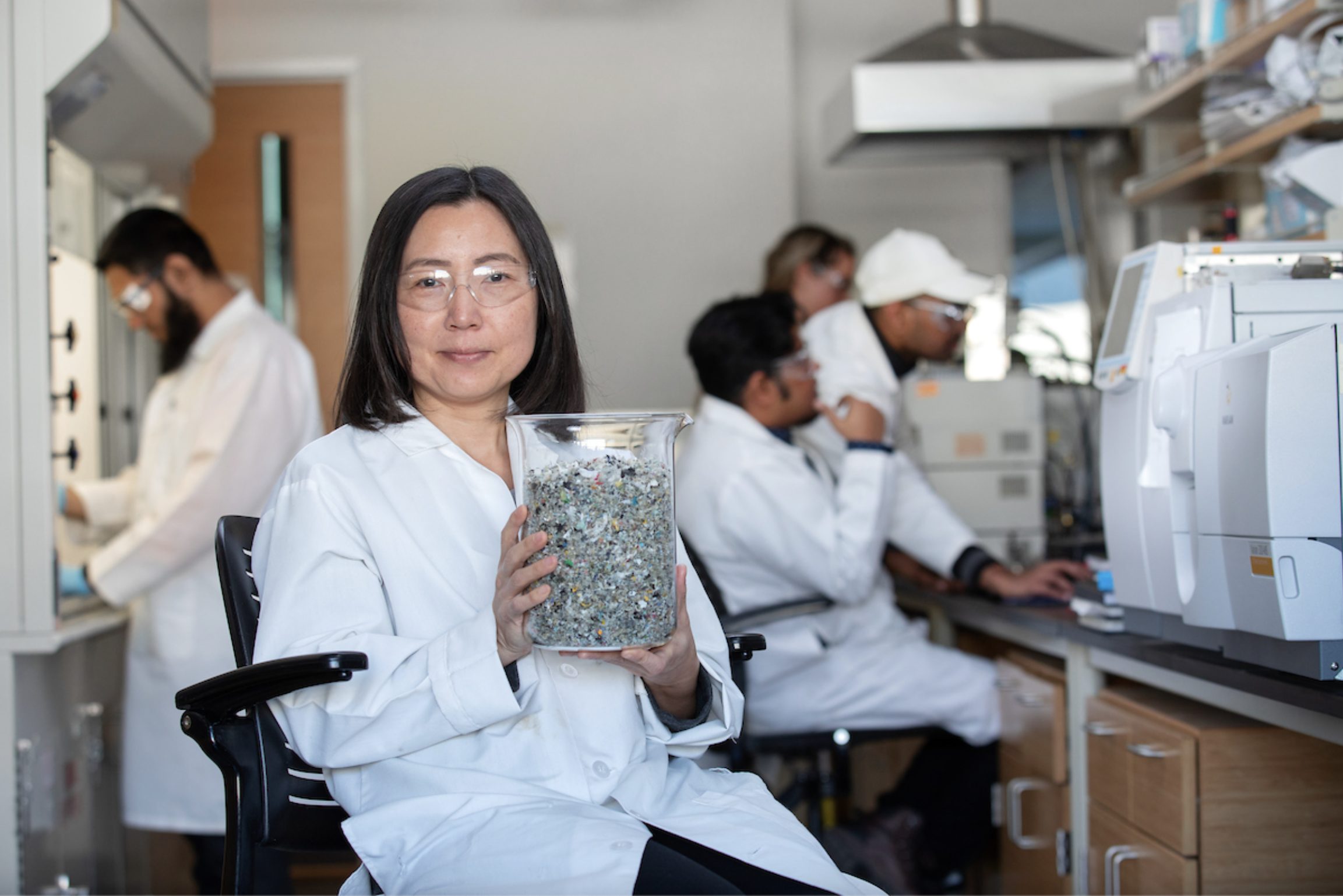 A young lady examines a printed microchip underneath a hood as part of a research experiment. Another female researcher can be seen in the background of the shot.